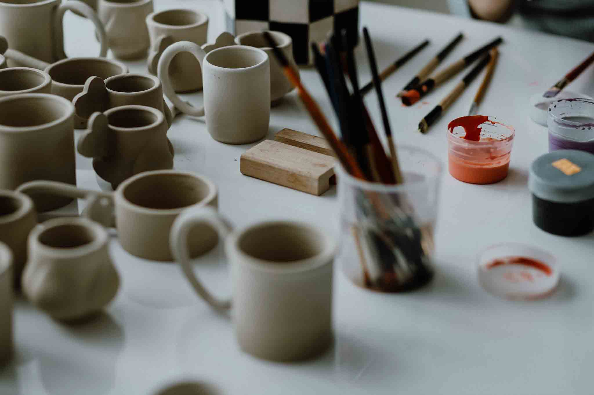 Different pottery tools and unpainted ceramic vessels on a workspace.